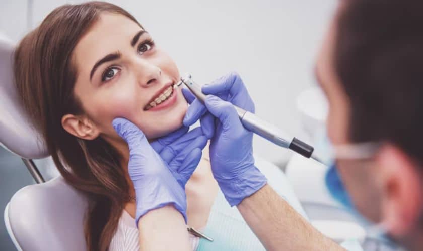 Dentist in blue gloves examining smiling female patient's face during dental consultation in clinic.