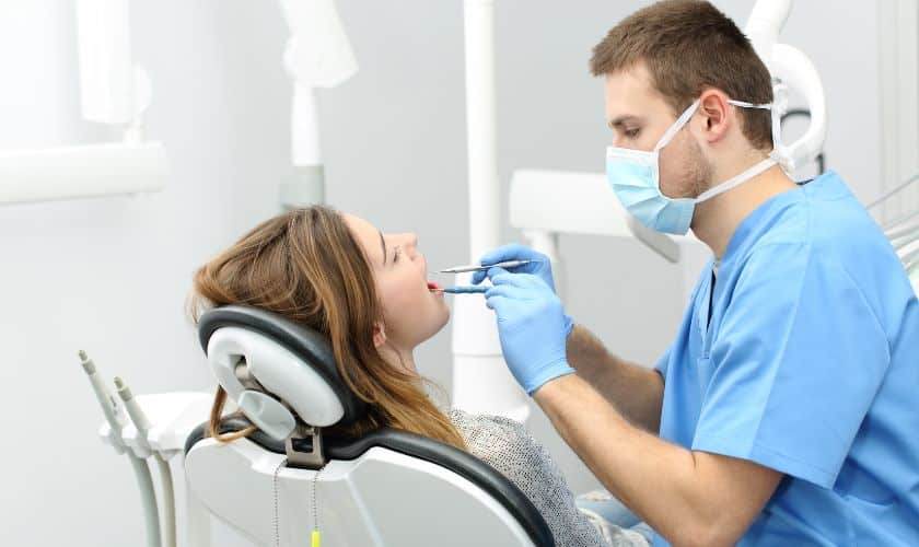 Dentist in blue scrubs examining patient's teeth in modern dental clinic office.