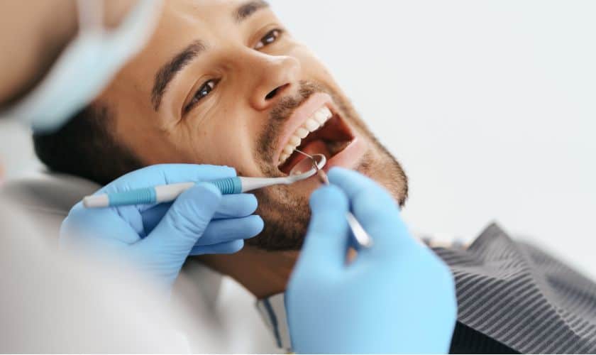 Dentist in blue gloves examining patient's teeth during dental checkup at clinic.