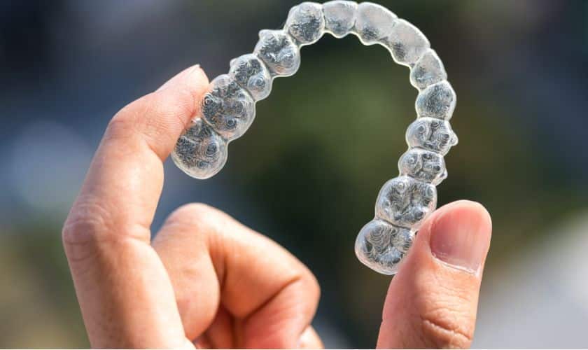 Person holding clear plastic dental aligner or retainer in hand outdoors.