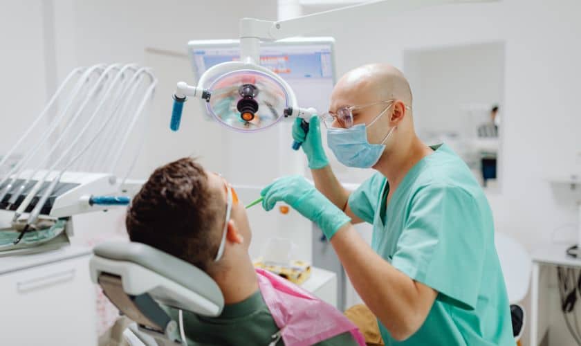 Dentist examines patient's teeth in modern dental clinic operatory with assistant present.