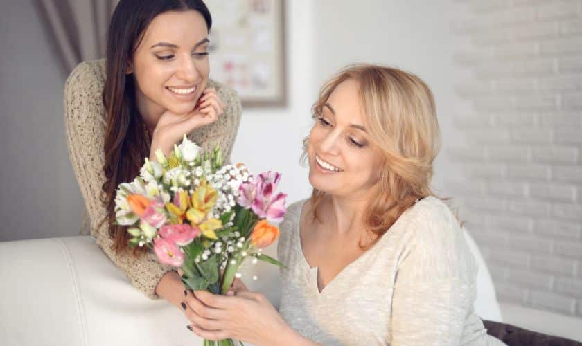 Two women smiling while holding a colorful flower bouquet in a bright, modern dental office setting.