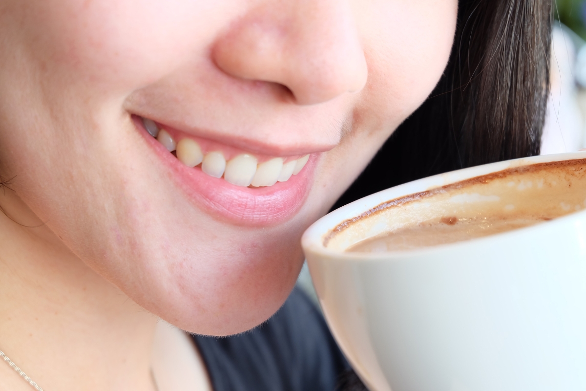 Close-up of a woman smiling while drinking coffee, showing early tooth discoloration and yellow stains caused by staining beverages