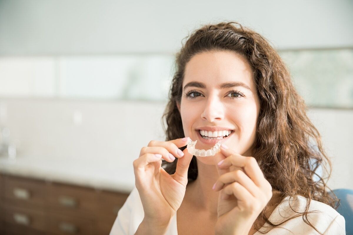 Woman holding clear aligner tray and smiling, demonstrating adult orthodontic treatment.