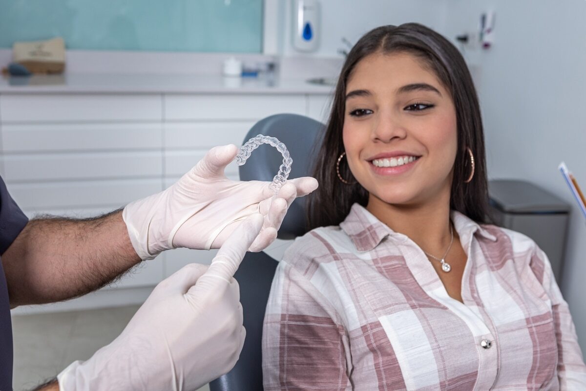 Patient smiling while dentist displays clear aligner tray in dental office.