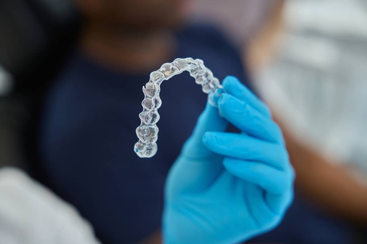 Clear orthodontic aligner held in a gloved hand, showing dental treatment tool for cavity prevention.