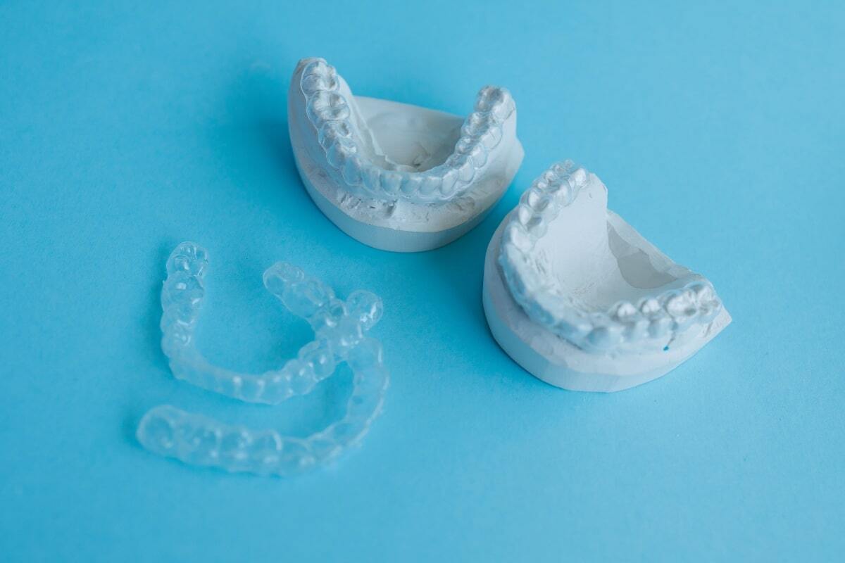 Clear dental aligners next to white plaster teeth models on blue background.